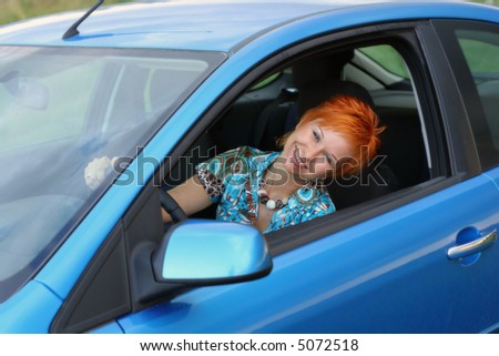 Young red-haired woman is siting in a blue car. Woman is happy