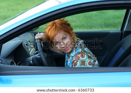 Young red-haired woman is siting in a car. Woman is happy