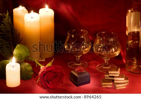 Valentine dinner with rose, candles, gift box, candies and two glasses of white wine on carmine velvet background.