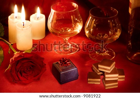 Valentine dinner with rose, candles, gift box, candies and two glasses of white wine on carmine velvet background.