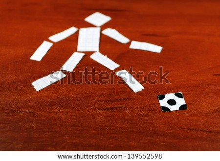 Man\'s figure with a soccer ball from a writing-book leaf on the table