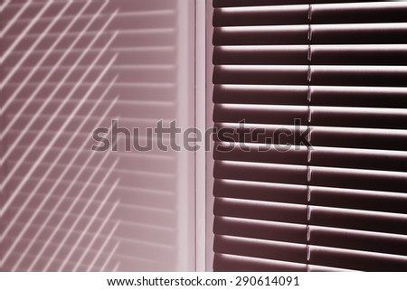 The corner of the window with the louvers at dawn with the reflected light strips that create a geometric pattern