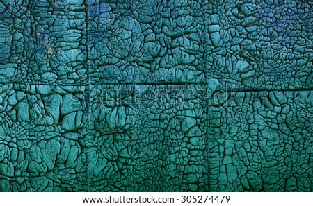 Old paint of green hue on square tiles made of plywood, flaking and chapped