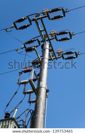 Energy and technology: electrical post by the road with power line cables, transformers against bright blue sky providing copy space.