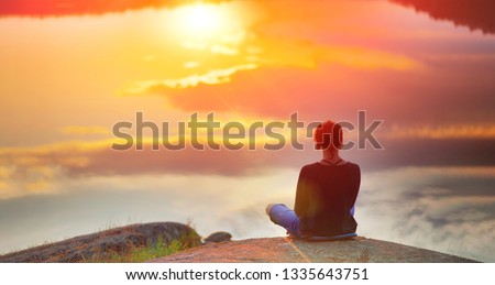 Beautiful woman sits in a pose of a  lotus on high place with amazing view of the lake sunset practice yoga meditation Kundalini energy mindset intuition prana. Solitude harmony mental freedom concept