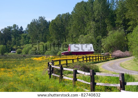 A red barn in a wildflower field with a fenced drive.