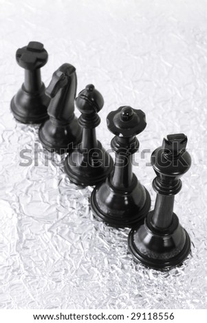 Black chess pieces on crumpled silver metallic texture background