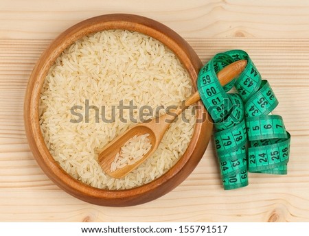 Raw rice in a bamboo bowl with tape measure over wooden surface