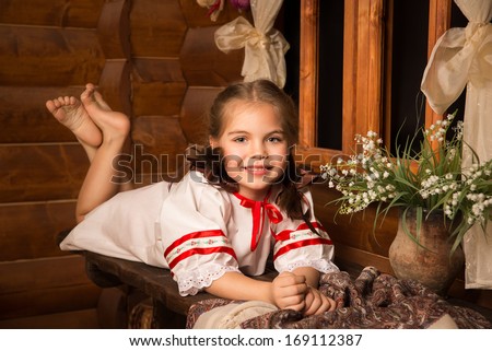 Girl in Russian national sundress. Folk dress.Cute little blonde girl in the hut. lying on the table next to the lilies of the valley