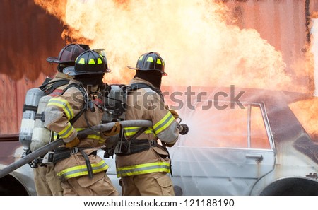 Three firemen extinguishing a car fire.
