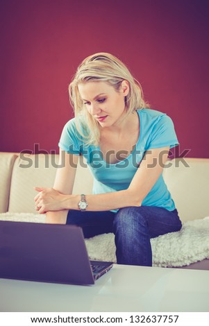 Pretty Young Girl Is Sitting at Home and Using Her Laptop (color toned image)