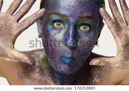 Beautiful face of a woman covered in glitter Close up of a woman\'s face covered in blue and purple glitter trying to scare you