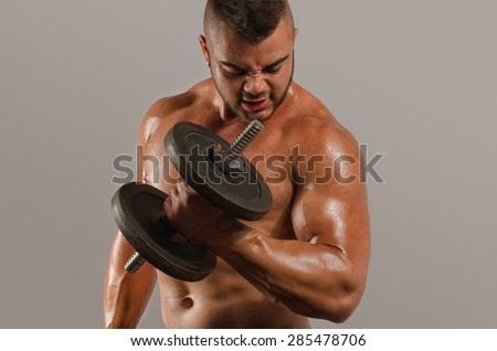 Strong bodybuilder man with perfect abs, shoulders,biceps, triceps and chest, personal fitness trainer training with heavy dumbbells, flexing his arms, getting his biceps big