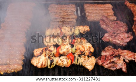 Delicious grilled meat with vegetable on a barbecue. Closeup of fried meat and sausages on a grill with smoke.