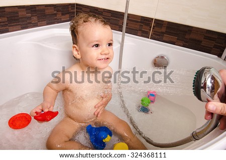 Toddler taking a bath. Little baby in a bathtub, mother\'s hand washing his hair with shampoo and soap. Kid playing with foam and water splashes. Clean kid after shower. Child hygiene