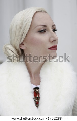 Beautiful blond woman in a white fur  coat and red medallion on a white background with a tidy hairstyle