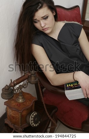 girl reading book in old flat and waiting by the an old telephone , Portrait of attractive woman waiting call by old-fashion phone at black background