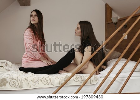two girls on the bed happy dreamy beauty girl hugging her legs while siting in bed against the wooden wall
