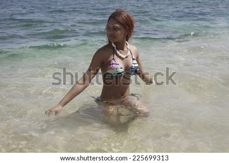 Latina in bikini playing in water, girl in swimsuit wearing necklace walking out of water on sandy beach