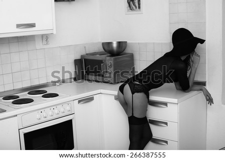 girl with a belt for stockings in the transparent body standing in the kitchen, black and white photography