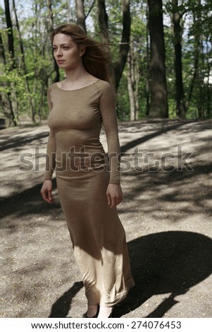 blond girl with long golden dress standing in the woods