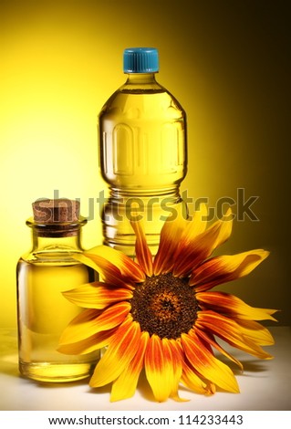 Cooking oil in a plastic and glass bottles with sunflower on a dark yellow background.
