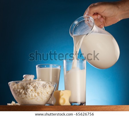 Man hand pouring milk from jar into the glass. Isolated on a  blue.