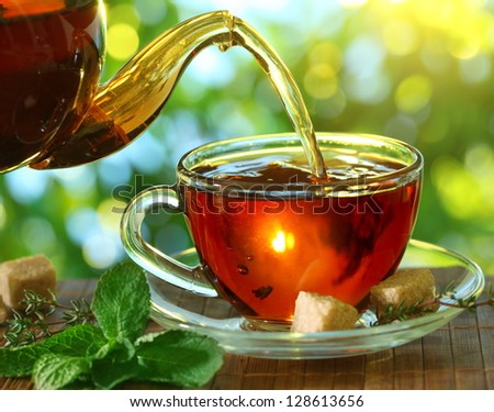 Pouring tea from a teapot into a cup on a blurred background of nature.