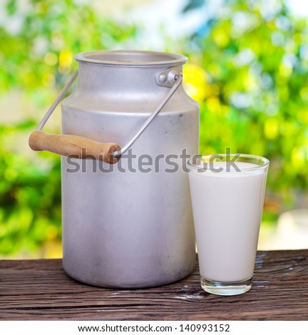 Milk in aluminum can and glass on the old wooden table on outdoor setting.