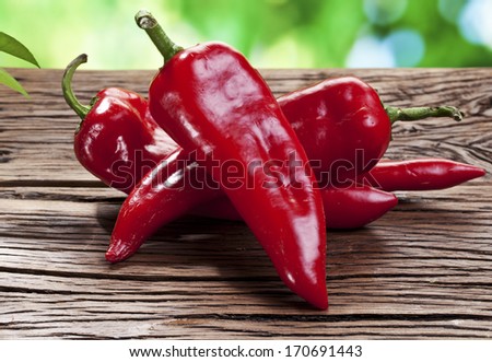 Red peppers on a wooden table with green foliage on the background.
