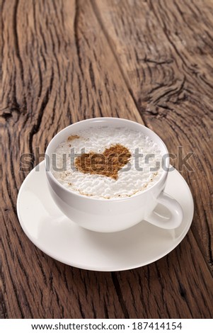 Cup of cappuccino with ground cinnamon in the form of heart on old wooden table. Top view.