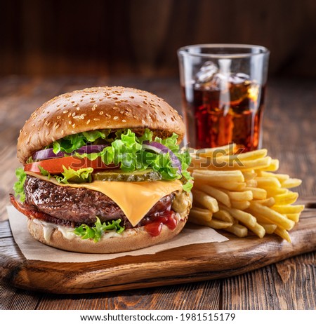 Delicious hamburger with cola and potato fries on a wooden table with a dark brown background behind. Fast food concept.