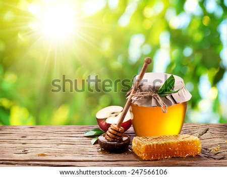 Glass can full of honey, apple and combs on wooden table at the nature background.