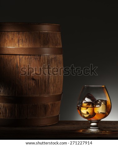 Glass of matured whiskey with ice cubes in it and old wooden barrel.