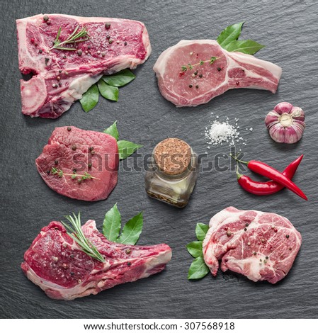 Raw meat steaks with spices on the black cutting board.