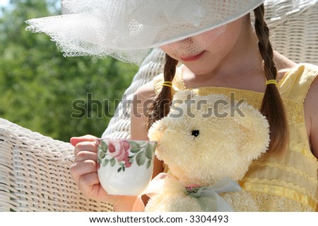 little girl in wicker chair having tea party with teddy bear
