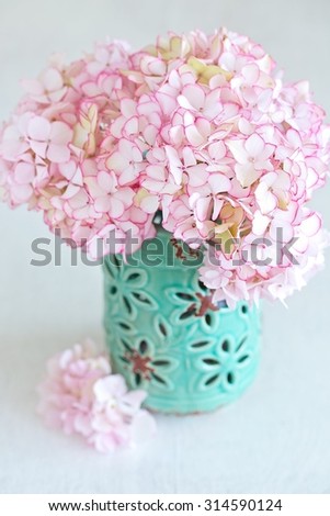 Beautiful pink hydrangea flowers in a blue ceramic vase on a light background.