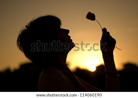 Silhouette of a woman holing a flower at sunset