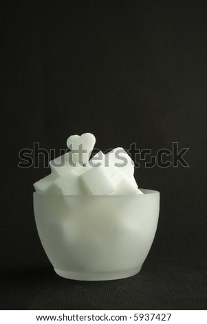 A translucid bowl of white lump sugar, on a black background.