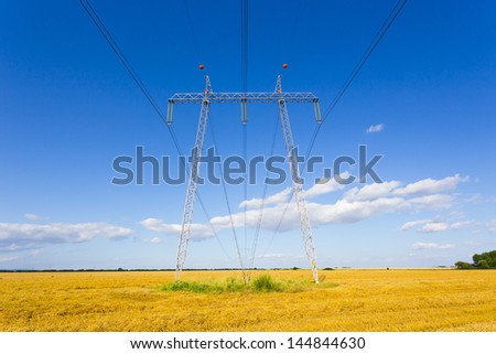 high-voltage lines on harvested wheat field with blue sky in summer