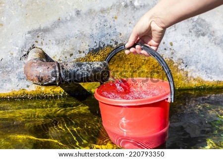 fresh drinking water and red plastic bucket in hands of a woman