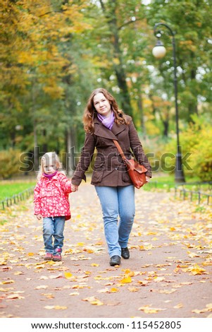 Beautiful mother and daughter walking in autumn park together