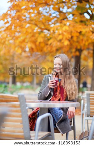 Smiling young lady drinking mulled wine in an outdoor cafe in a Parisian park