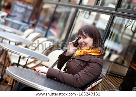 Happy young girl talking on cell phone in Parisian street cafe