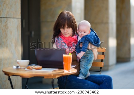 Young mother with her adorable baby boy working or studying on her laptop in cafe