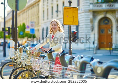 Beautiful young woman in red polka dot dress taking a bicycle for rent in Paris