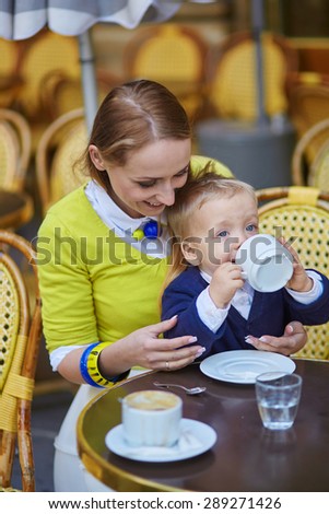 Happy family of two spending fun together in an outdoor Parisian cafe, little boy is drinking his beverage