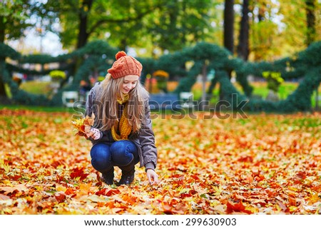 Cheerful young girl gathering autumn leaves in park
