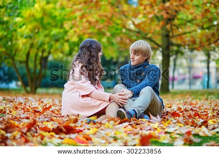 Young dating couple in Paris on a bright fall day sitting on the ground in autumn leaves