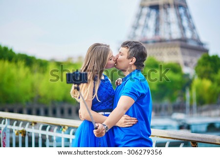 Romantic dating couple on a bridge over the Seine in Paris, taking selfie using selfie stick and kissing, Eiffel tower is in the background